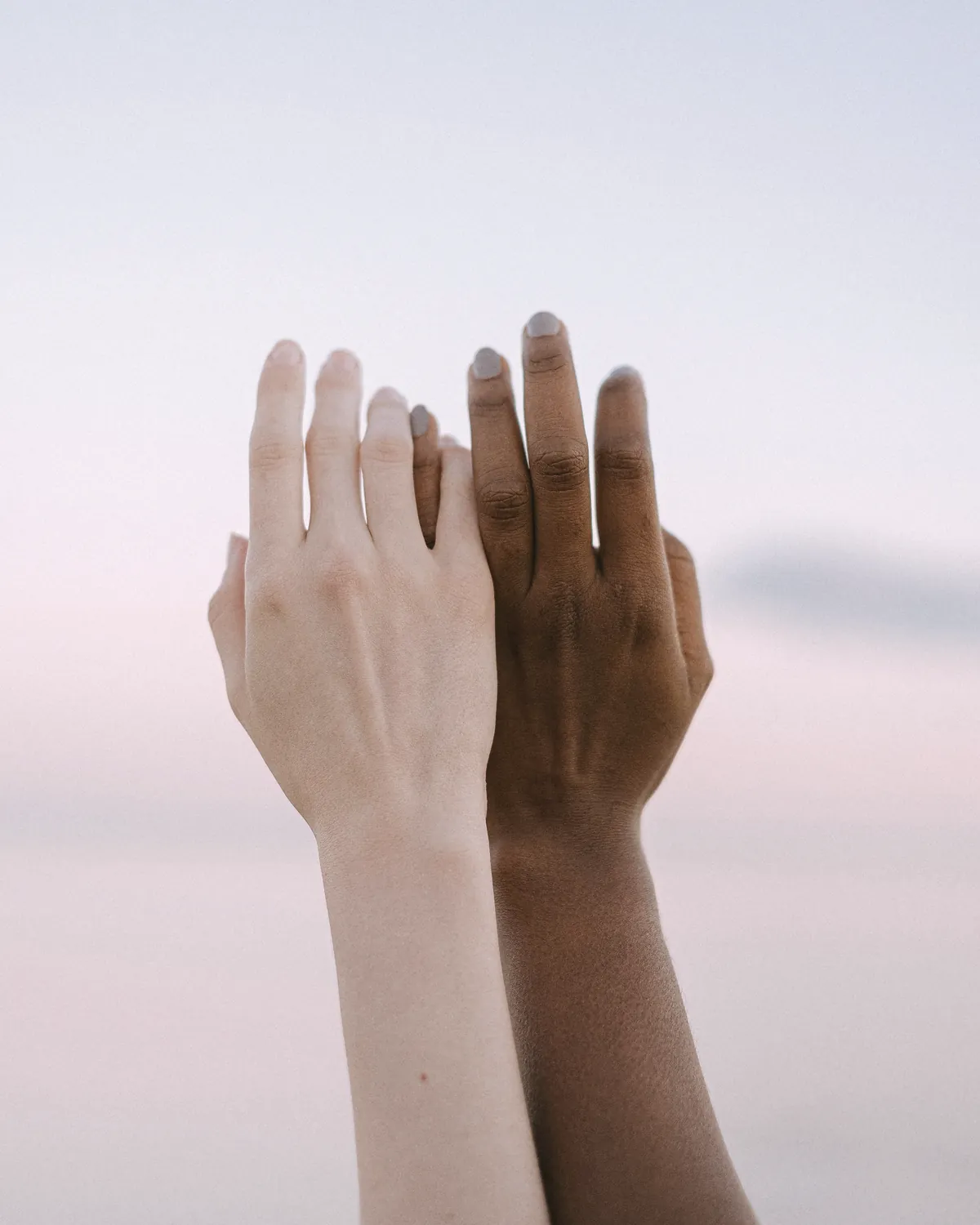 Two hands reaching towards a clear sky
