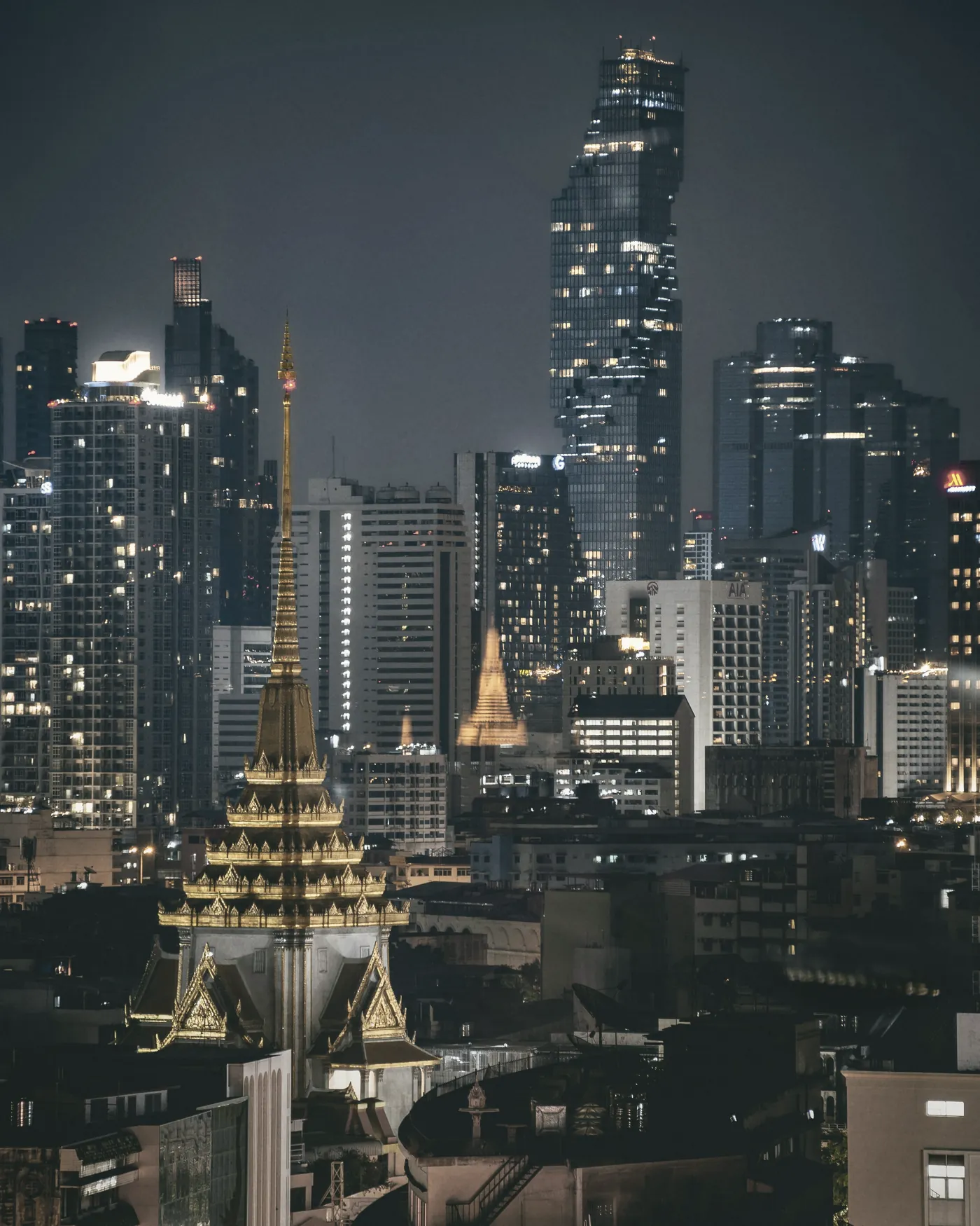 A golden temple spire in front of Bangkok's skyscrapers at night