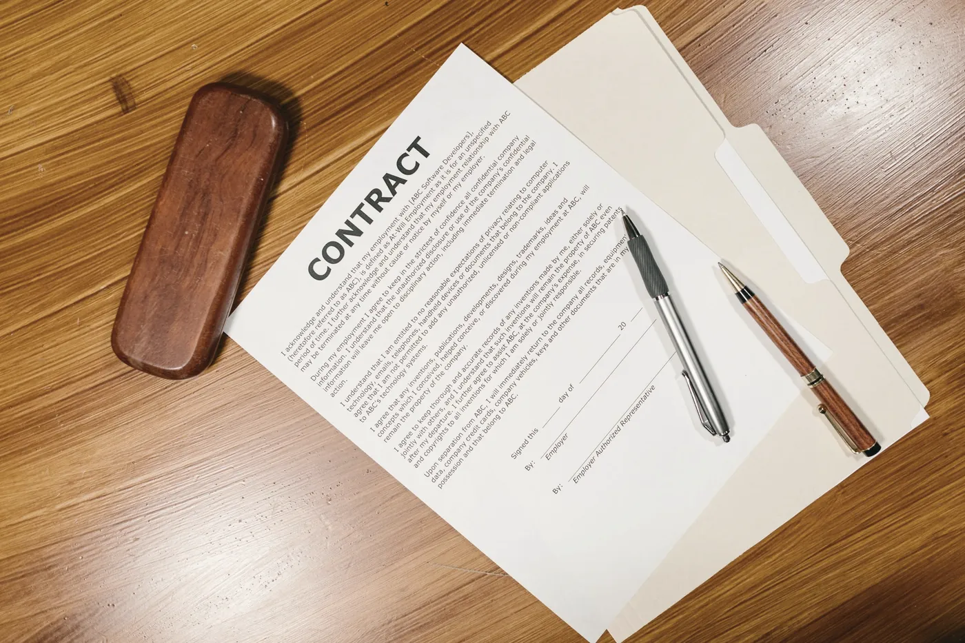 A document, a pen and a glasses case on a wooden desk