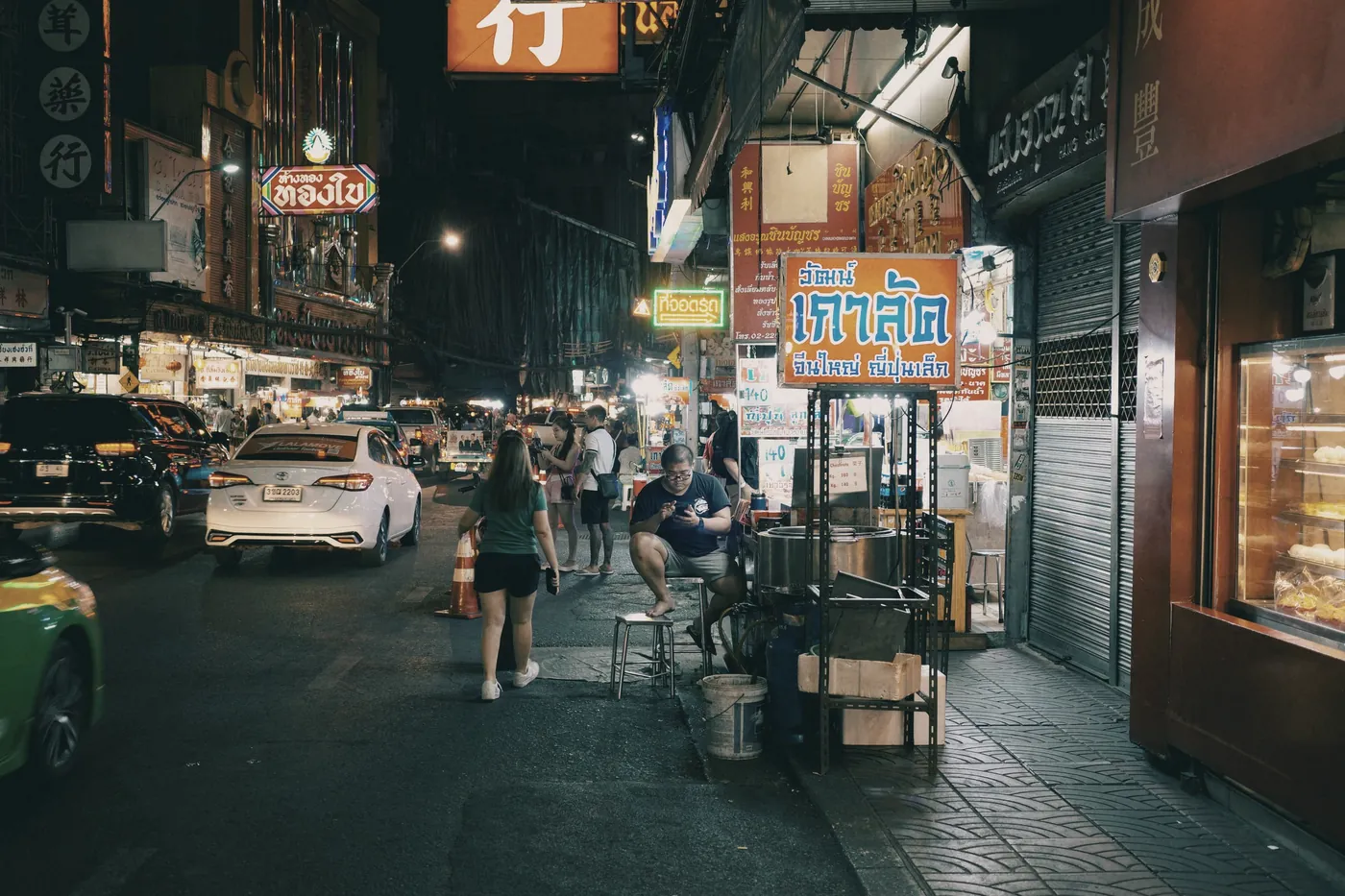 A Bangkok street at night lined with lit-up shopfronts