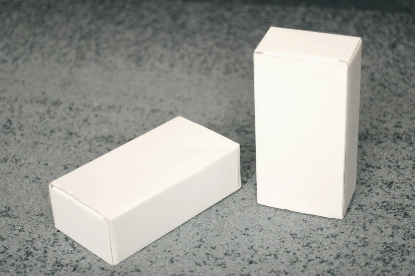 Two plain white boxes standing side by side on a grey surface