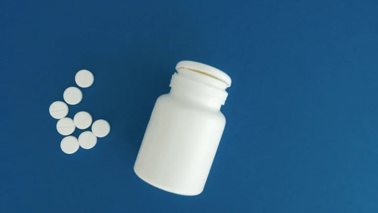 A white medicine bottle with loose white tablets on a blue background