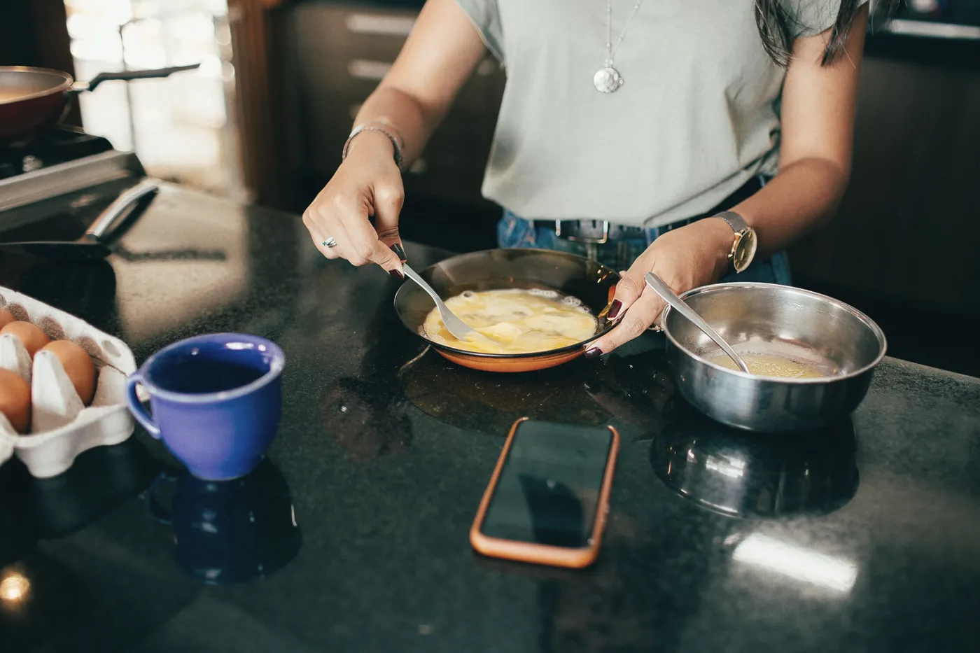 A phone on a kitchen counter while someone cooks at the stove