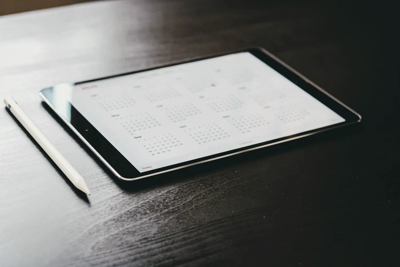 A tablet screen showing a monthly calendar beside a stylus