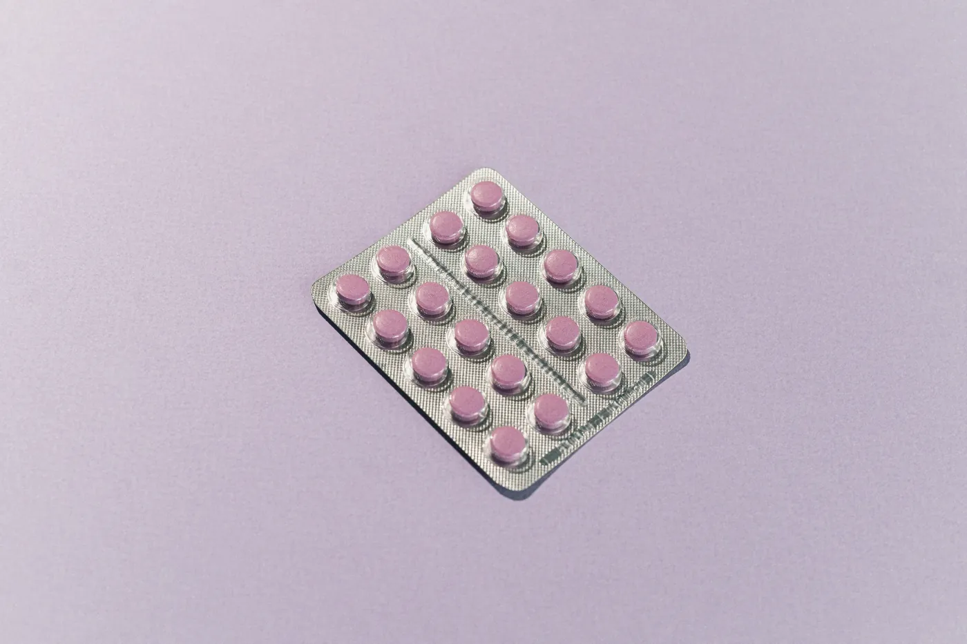 A blister pack of pink tablets on a lilac background