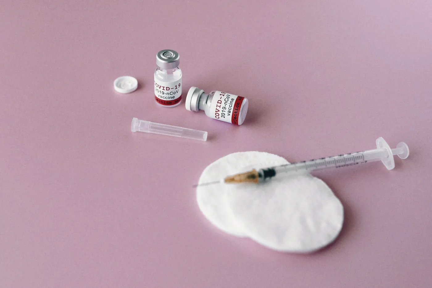 A small medicine vial, a syringe and a cotton pad on a pink surface