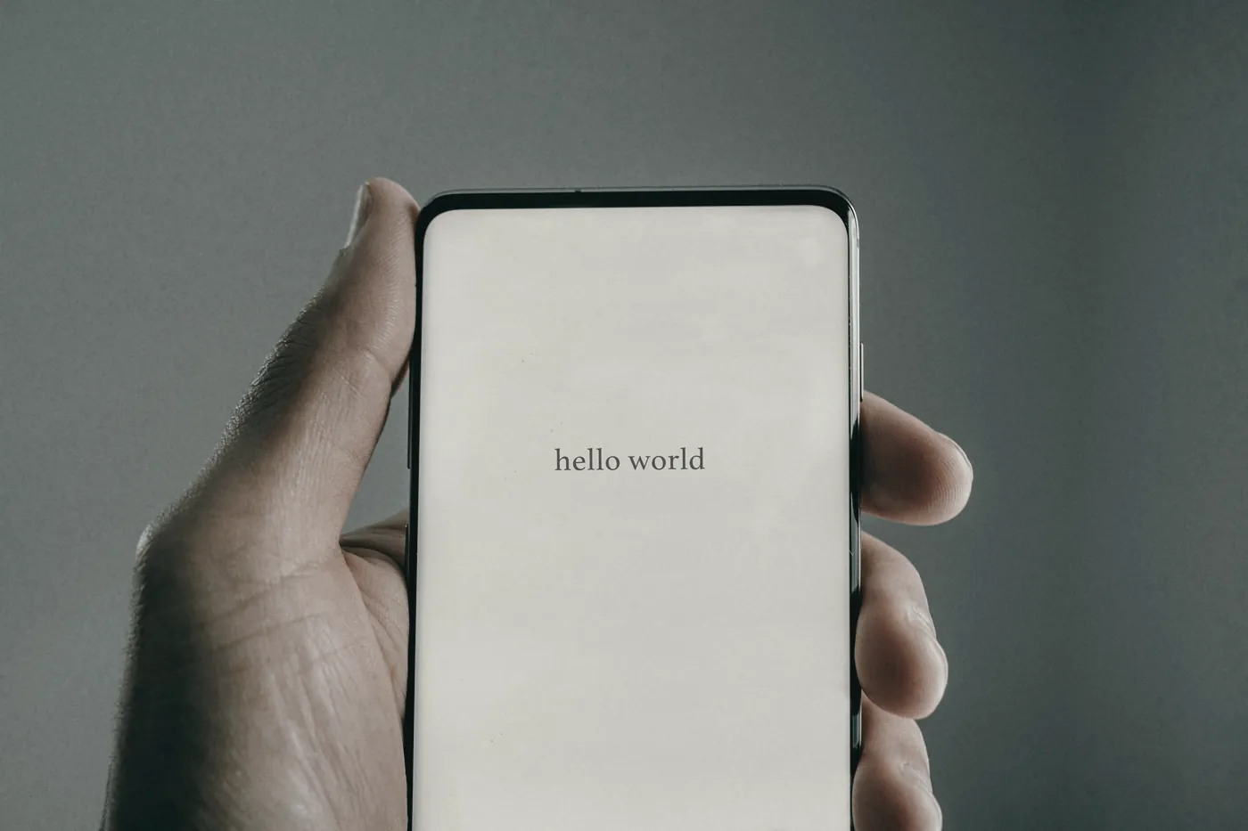 A hand holding a smartphone against a grey wall