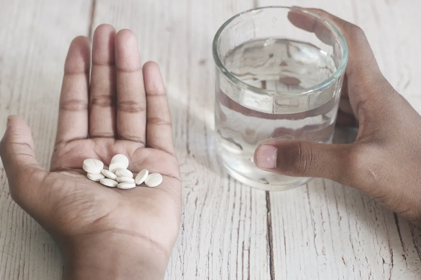 An open hand holding white tablets beside a glass of water