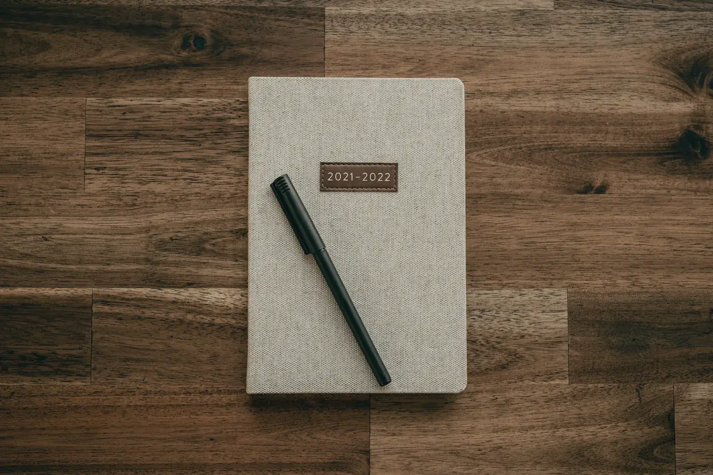 A closed notebook and a pen on a dark wooden desk