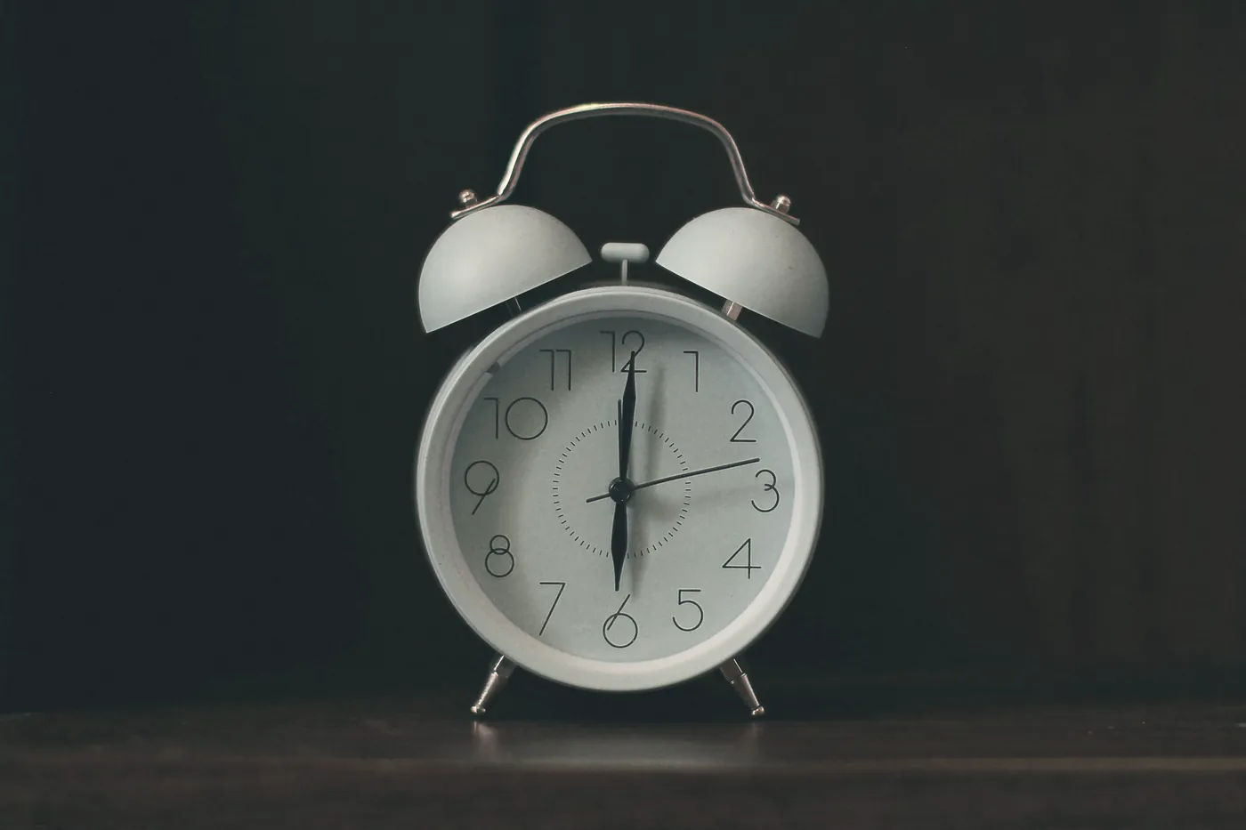 A white analogue alarm clock against a dark background