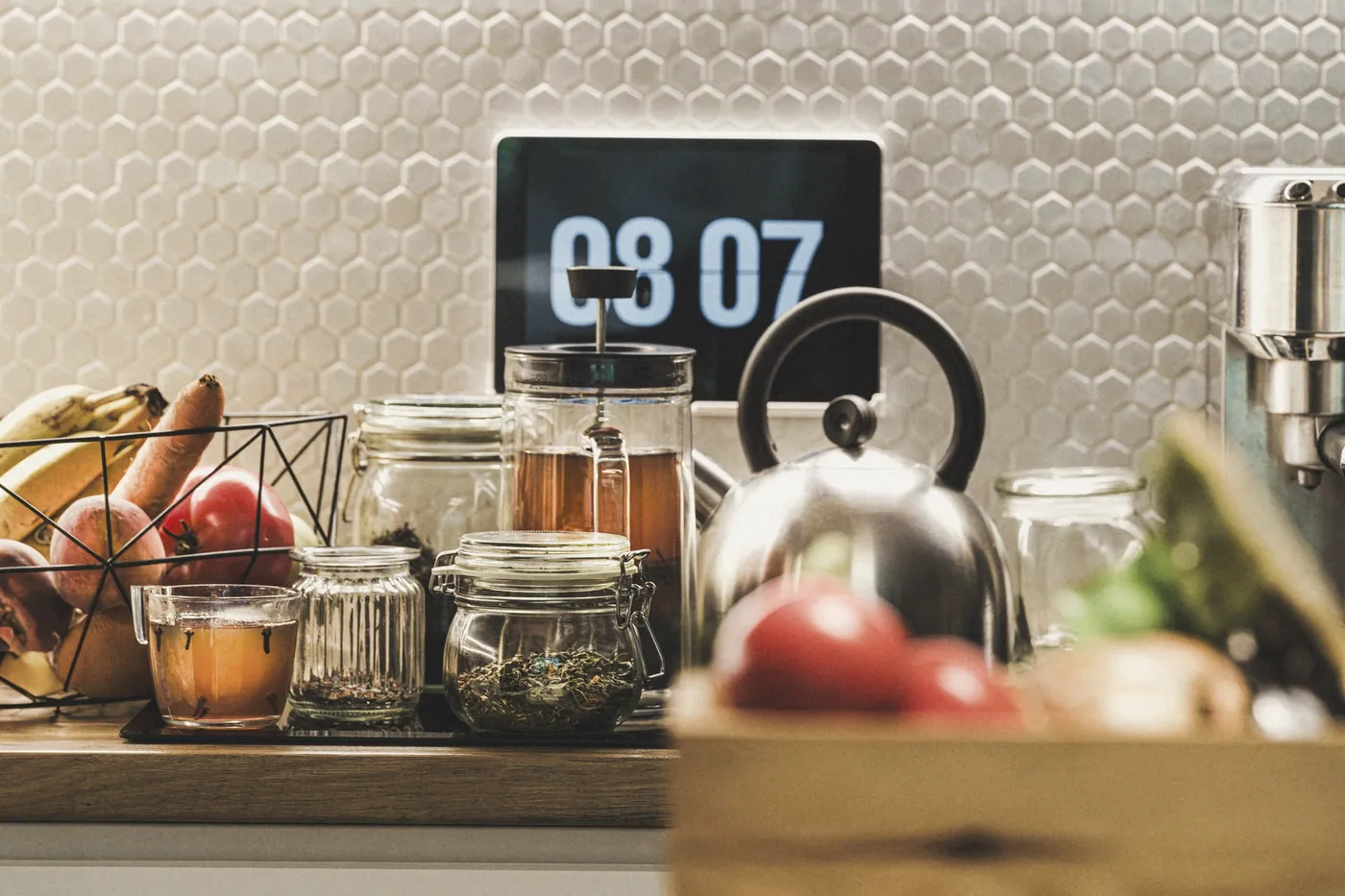 A kitchen counter with jars and a digital clock on the wall