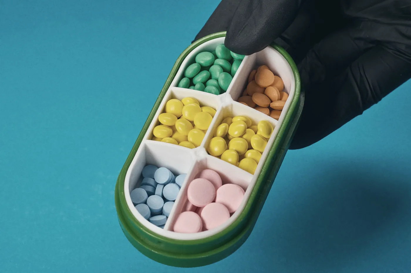 A hand holding a colourful pill organiser against a blue background