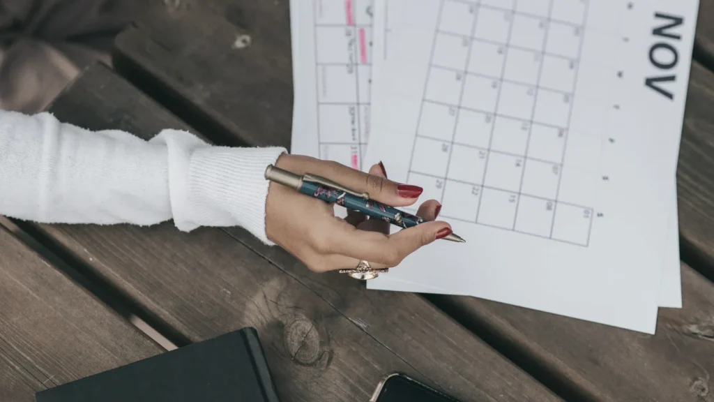 Hands holding a pen over a paper calendar while planning dates