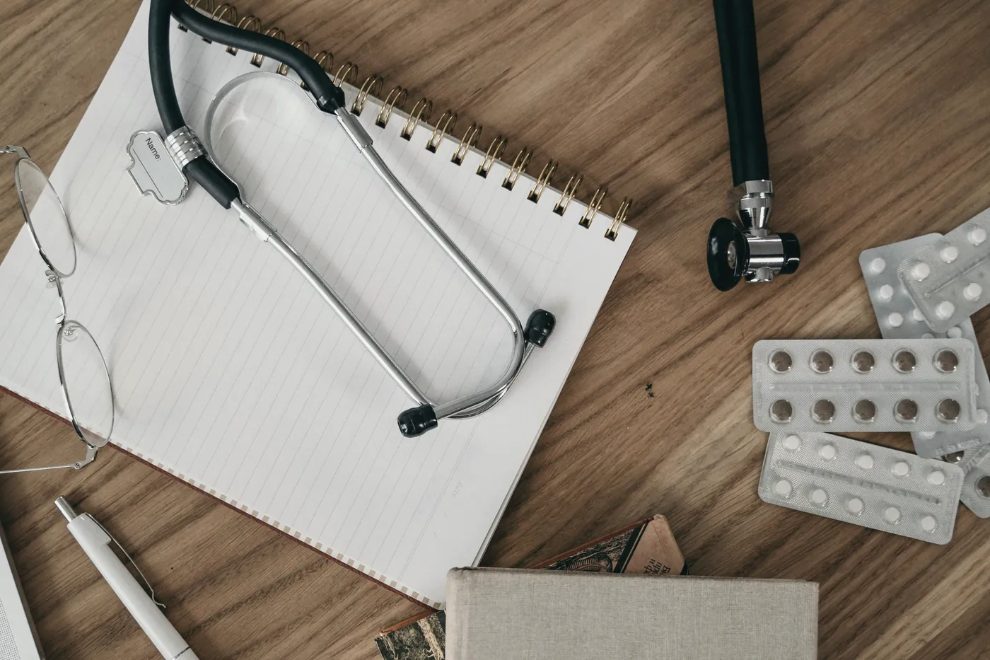 A stethoscope, a notepad and blister packs of tablets on a wooden desk