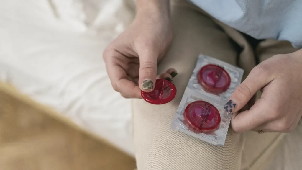 Hands holding condom packets on a white bed sheet
