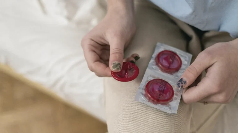 Hands holding condom packets on a white bed sheet