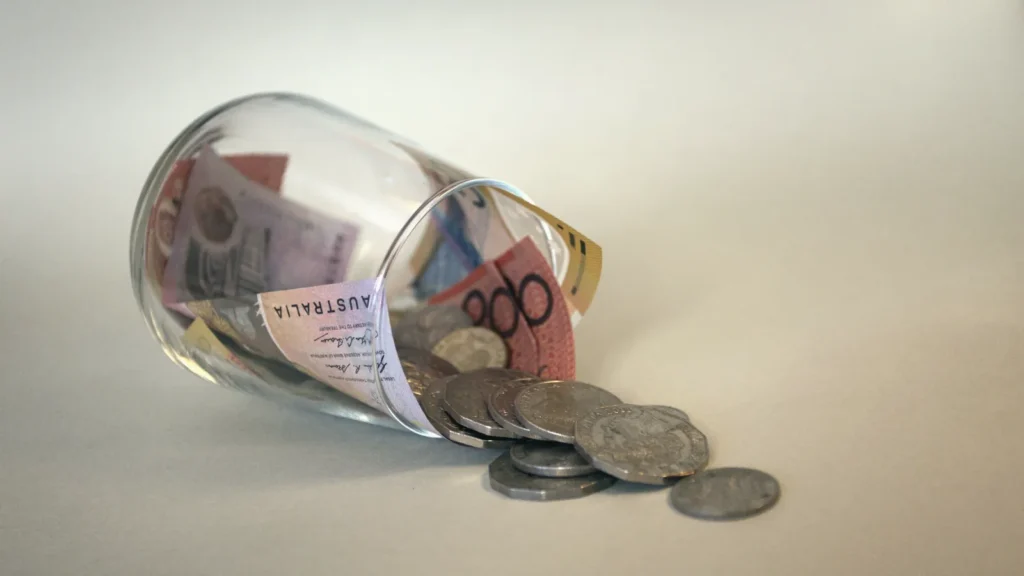 A tipped-over glass jar with banknotes and coins spilling out