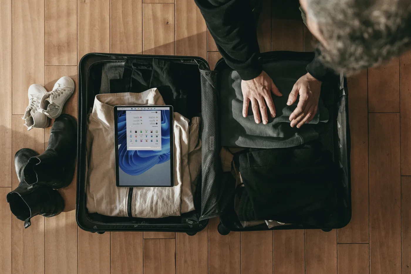 Hands packing an open suitcase on a wooden floor