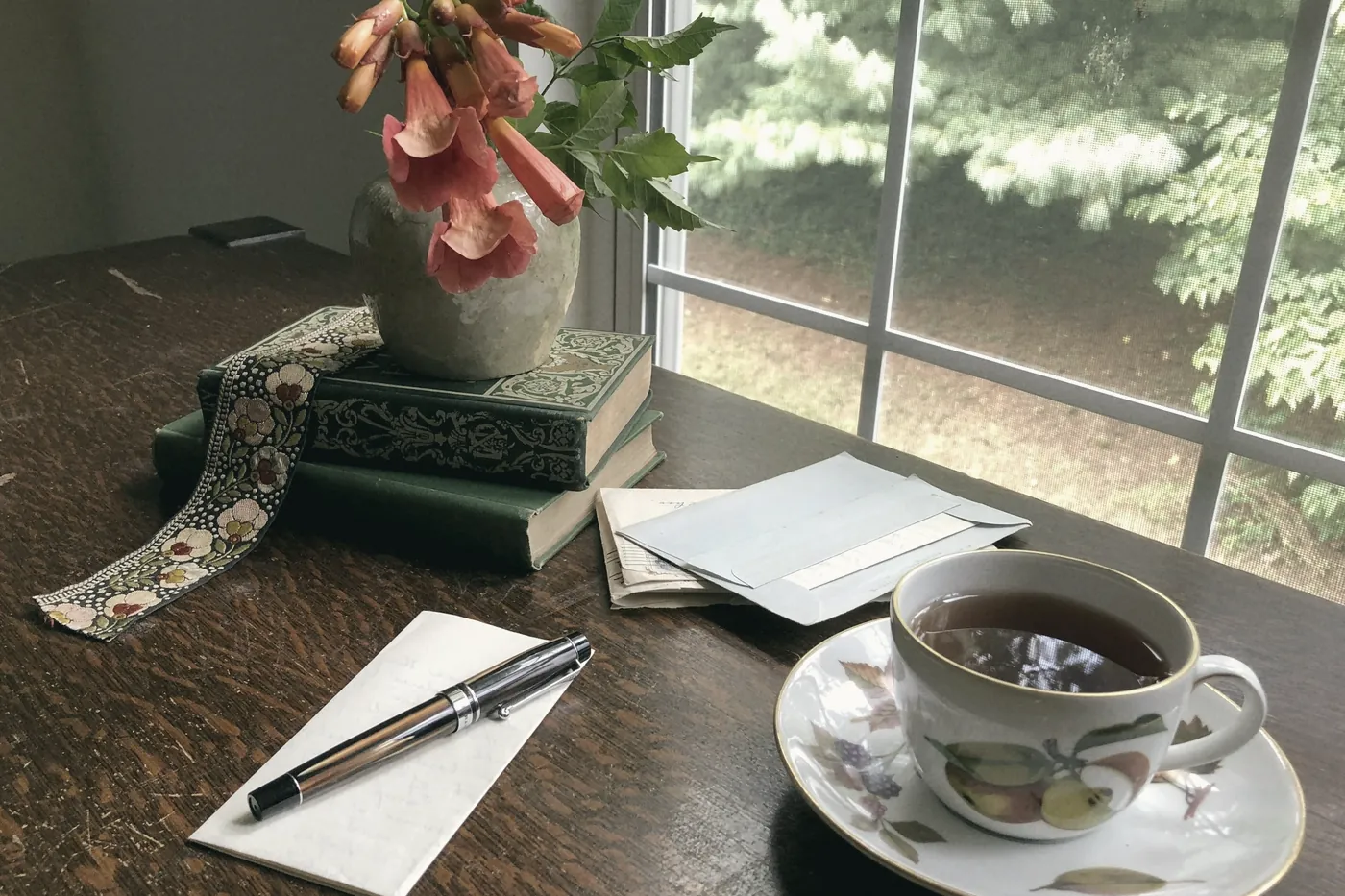 A cup of tea and a notebook on a desk by a sunny window