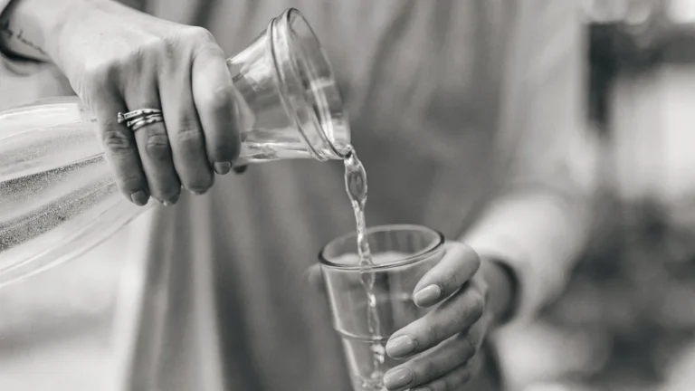 Hands pouring water from a glass jug into a drinking glass