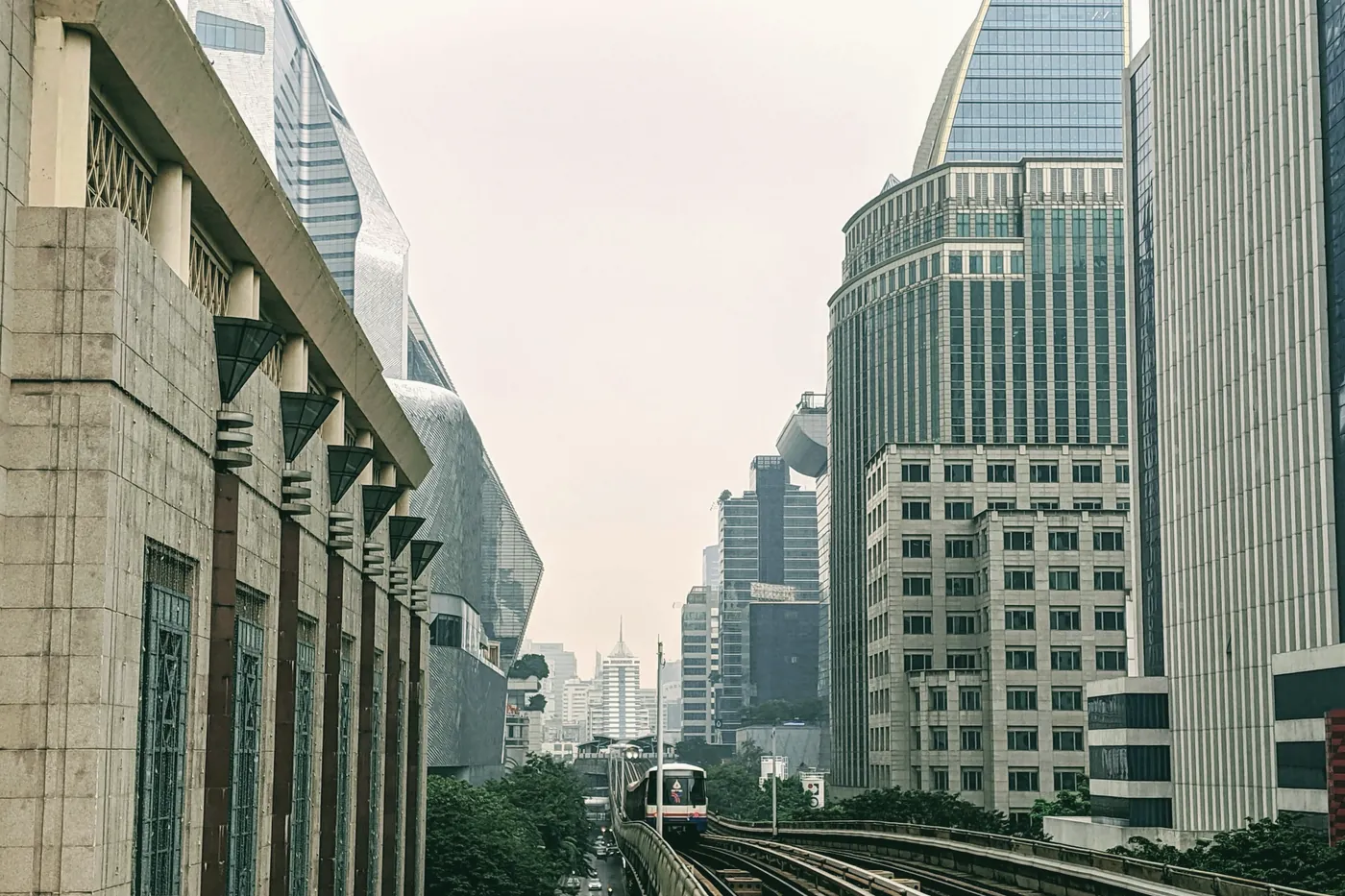 Elevated Skytrain tracks between Bangkok office towers in daylight