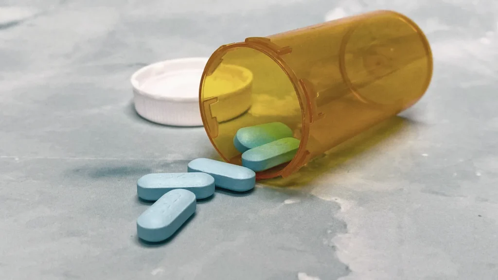 An orange pill bottle tipped over with a few blue tablets spilling out