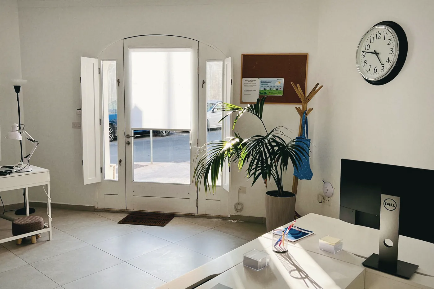A bright clinic room with a desk, plants and a wall clock