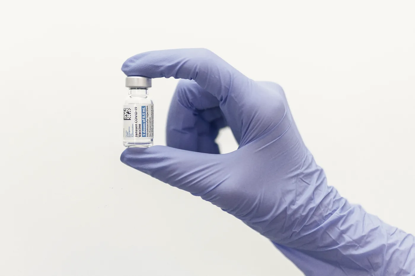 A gloved hand holding a small glass vial against a white background