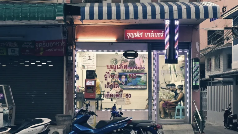A small Bangkok shopfront lit up at night with motorbikes parked outside