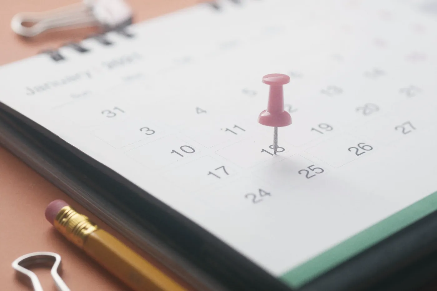 A red pin marking a date on a paper calendar