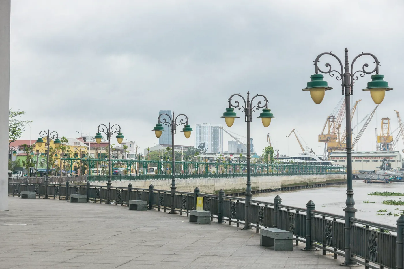 A riverside promenade in Bangkok with lamp posts and city towers