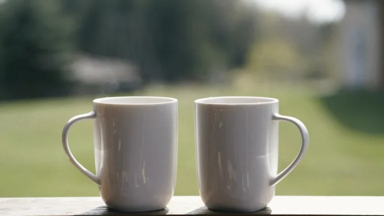 Two white coffee mugs side by side on a balcony railing